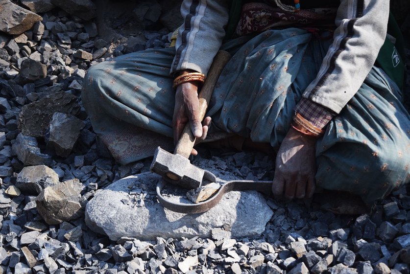 Woman breaking stones with hammer and clamp.