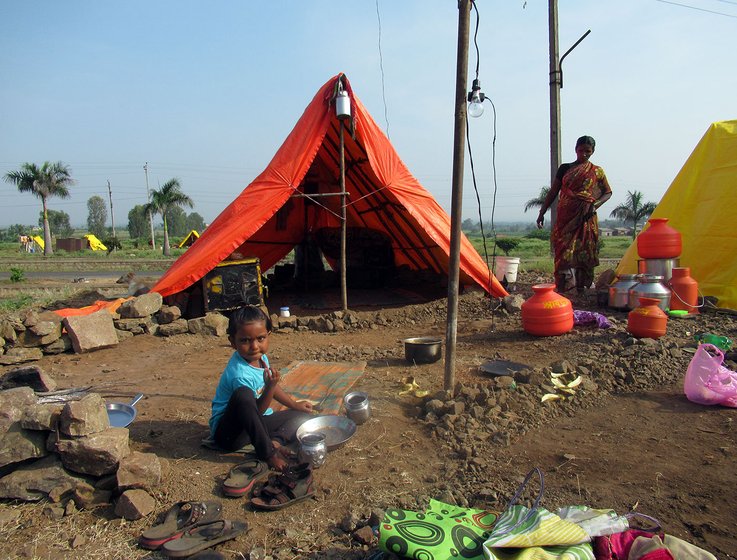 Young girl sitting outside a makeshift tent  as a woman looks on in the background