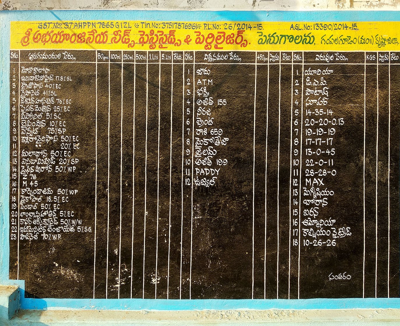 List of seeds, fertilizers and pesticides available in Abhayanjaneya Nursery, written on a wall.
