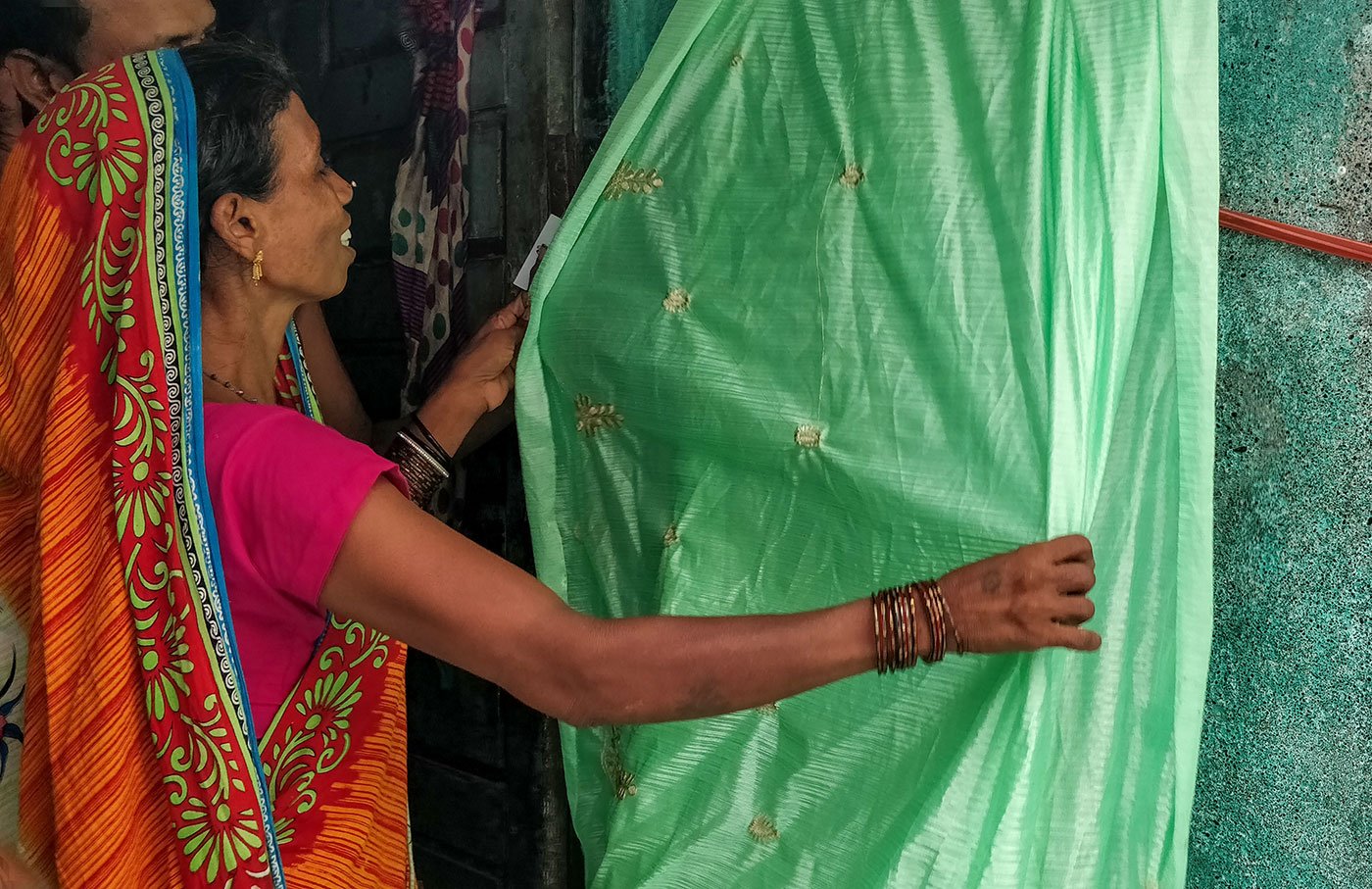 Shanti Sahu and her daughter Asha have fixed a rope outside their one room home in Mina Nagar to begin work on the saris that have been sent for the day. Shanti’s husband, Arijit, looks on.