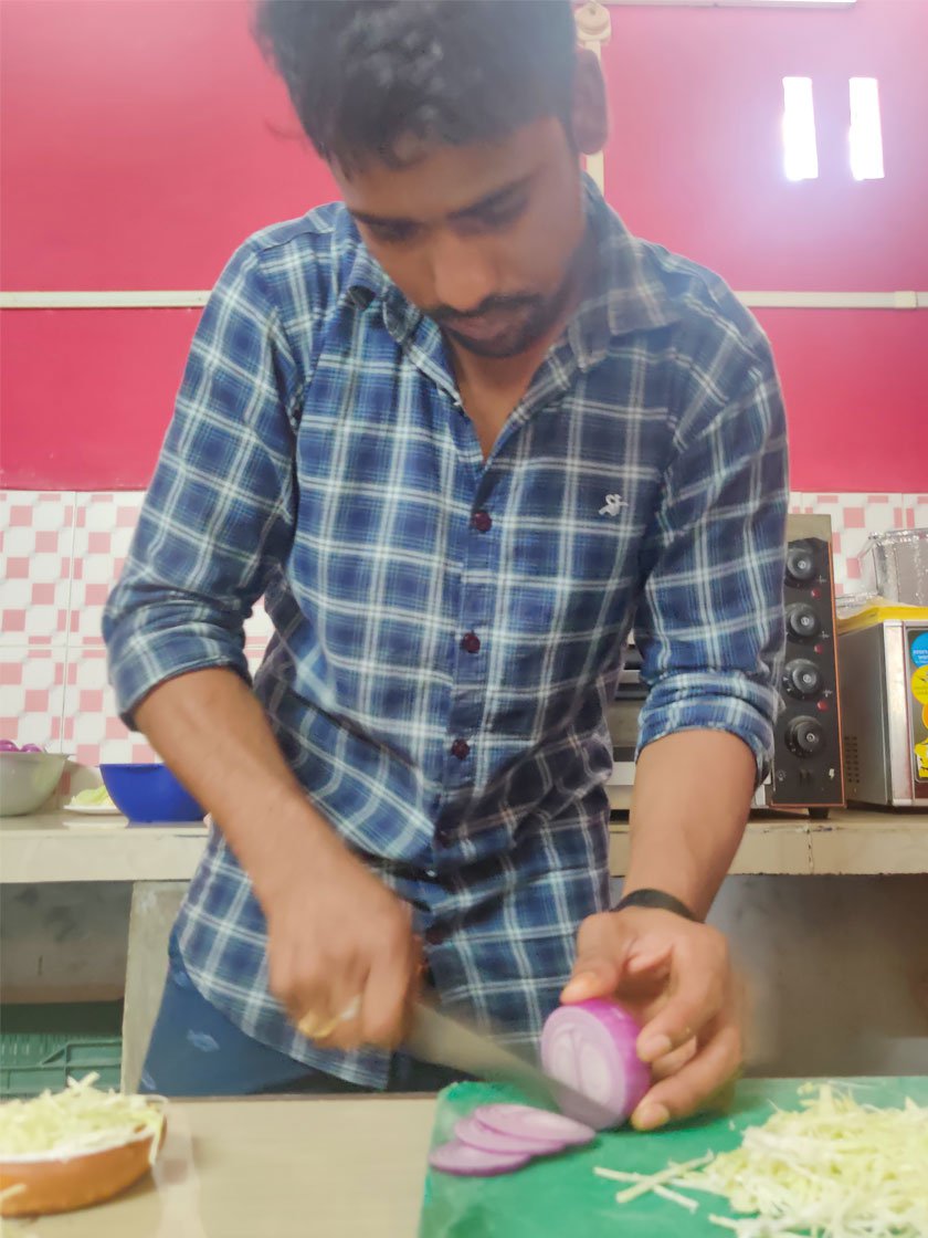 Biman dredging marinated chicken in flour (left) and slicing onions (right) to prepare a burger