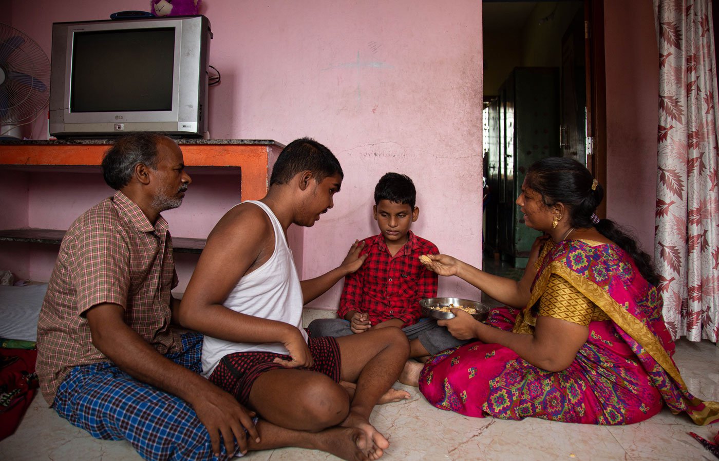 Saranya feeding her sons, M. Manase (right) and M. Meshak, with support from her father Balaraman. R (far left)