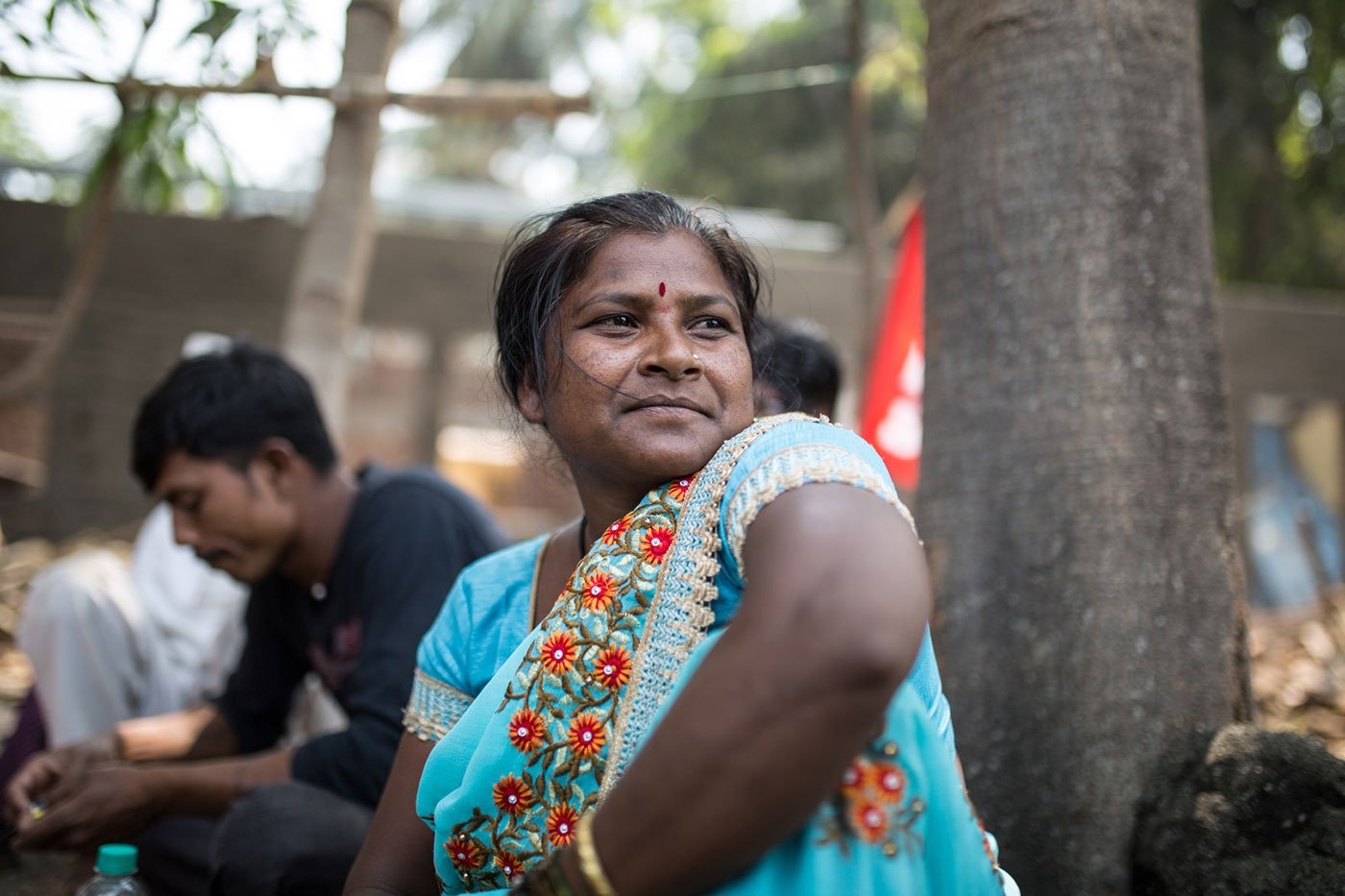 A woman sitting by a tree in a blue sari