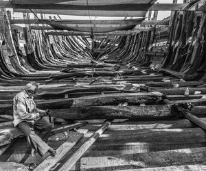A shipbuilder hammering the wood planks.
