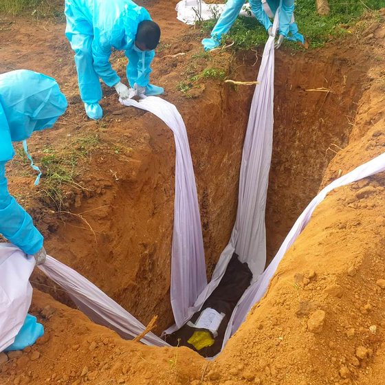 The volunteers lower a body into a pit eight feet deep, cover up the pit and pour a disinfectant powder across the grave

