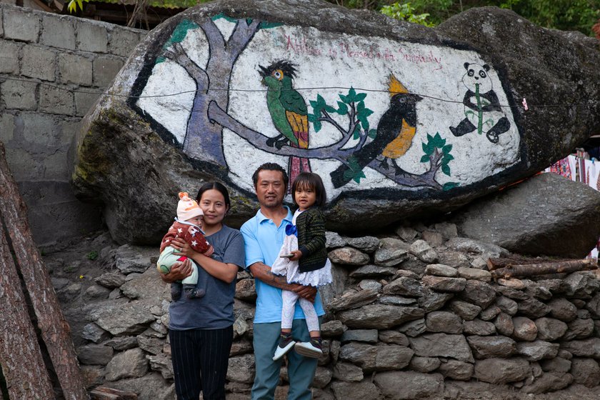 Leki Norbu and his family outside his home in Singchung. Behind them are paintings of the Bugun Liochicla (left) and another passerine, the Sultan Tit (right)