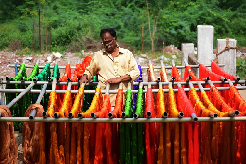 The spun yarn is separated to the length of the sarees and dyed in bright colours-- cotton candy pink, parrot green. It takes 2-3 days to prepare the dyed yarn. The labourers who dye the yarn are usually hired as a team of three persons, and each dyer earns Rs. 200 a day on the days they are called in to work. Arunachalam Perumal, 58, drying the yarn. He has been in this industry since he was 12 years old 