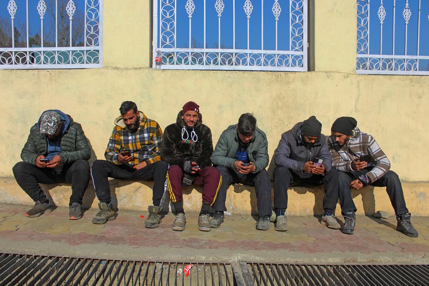 Employees of clothing rental shops watch videos on their mobile phones (left) or play cricket in a nearby ground as they wait for work