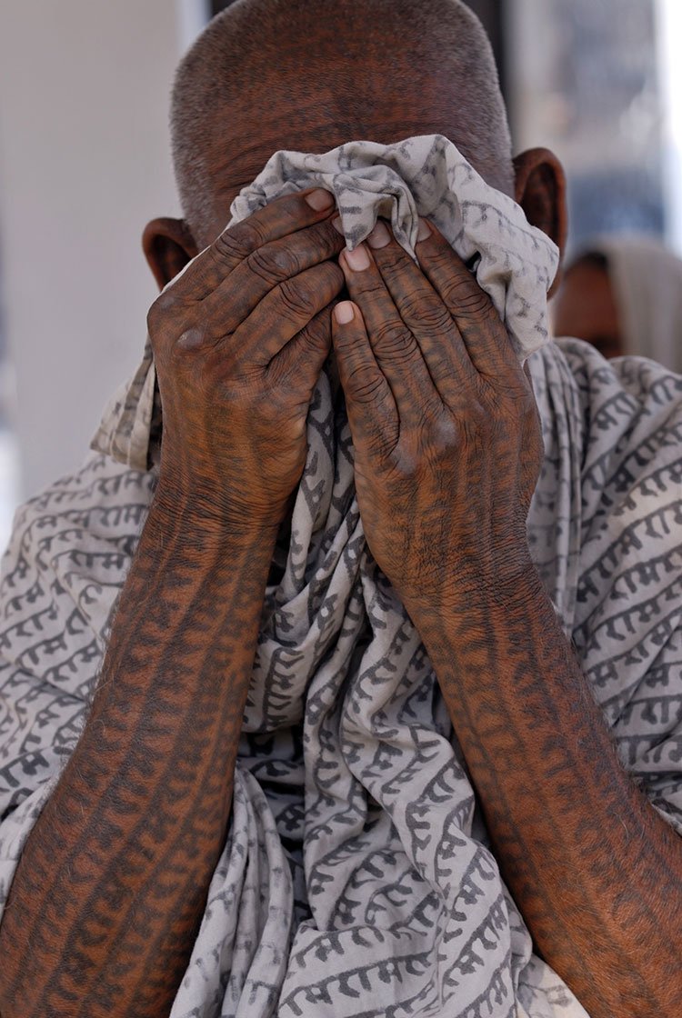 Old man covering his face with a shawl that has Ram's name printed all over it