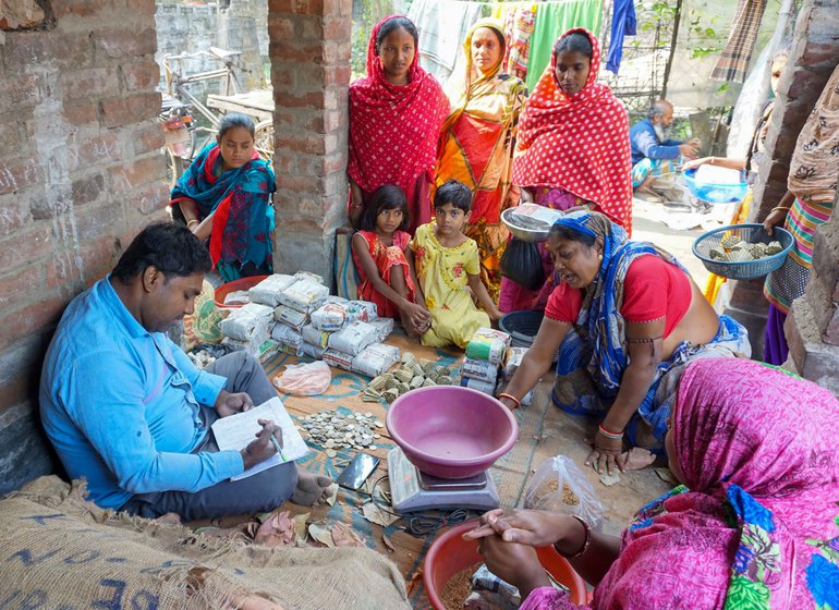 A mahajan settling accounts in Tanuja Bibi’s yard; Tanuja (in a yellow saree) waits in the queue.