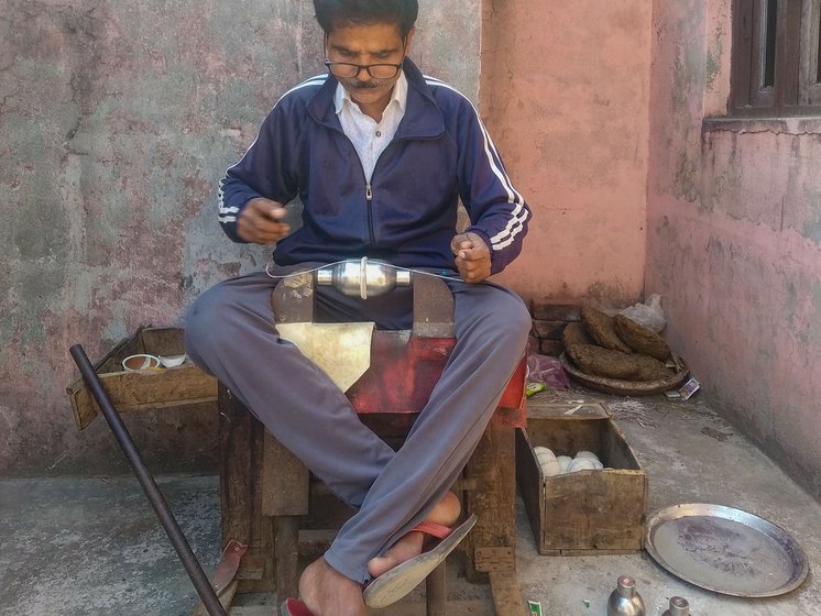 Bharat Bhushan using an aar to make insertions through the leather that protrudes between the two hemispheres, held together by an iron clamp. He places a rounded cork between the two cups and attaches pig bristles by their roots to the ends of a metre-long cotton thread for the second stage of stitching. He then inserts the two pig bristles through the same holes from opposite directions to stitch the cups into a ball