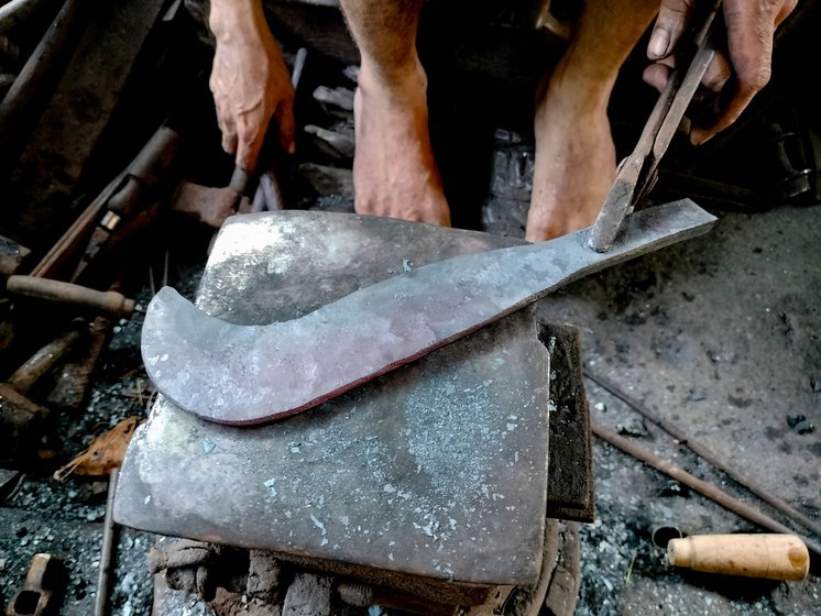 The veteran blacksmith is almost done shaping the sickle (left).