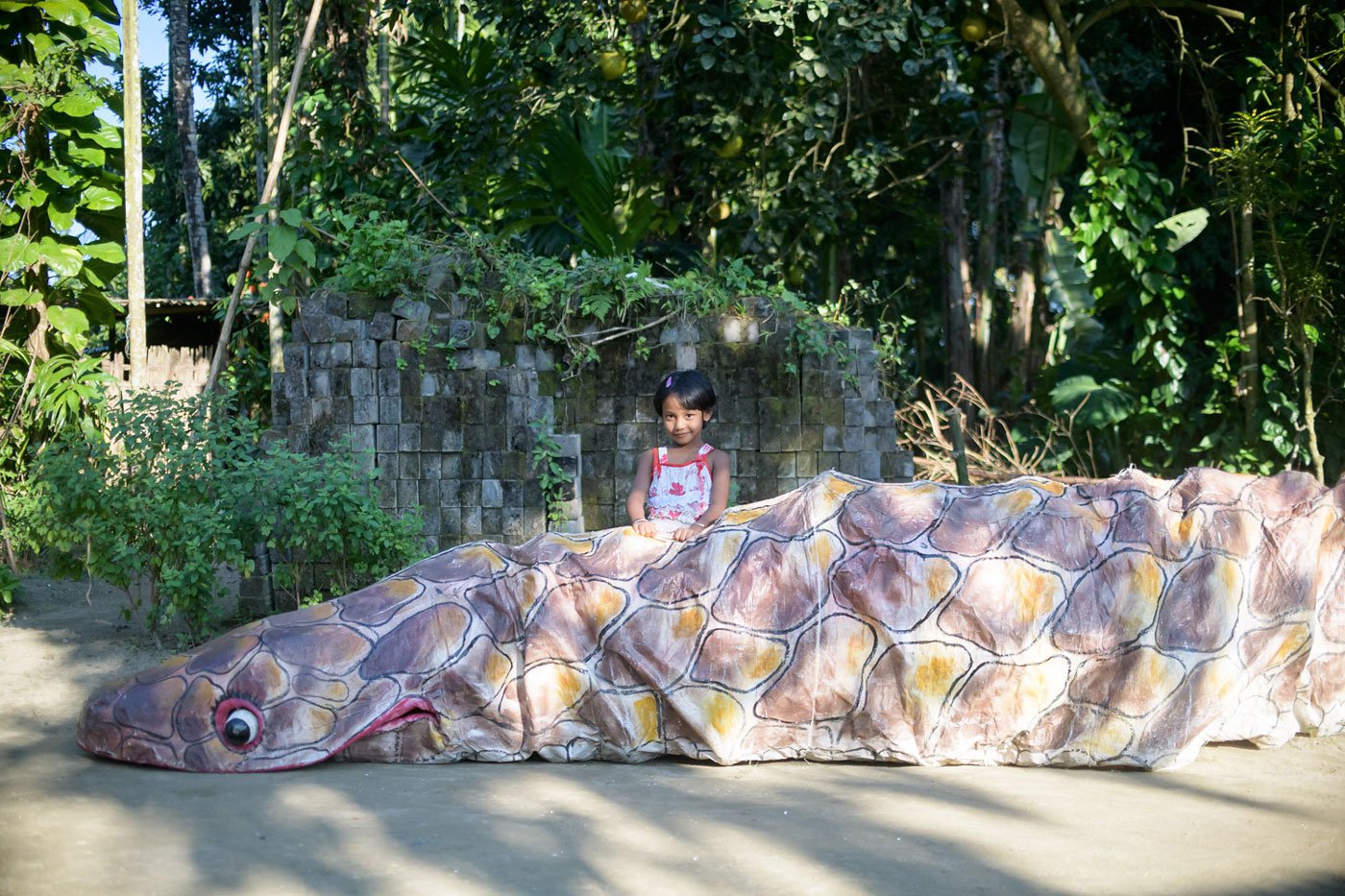 Anushka Dutta stands next to the giant Aghasura costume made by her father for the Raas Mahotsav. The six-year-old looks on as her father works on a project outside their home.