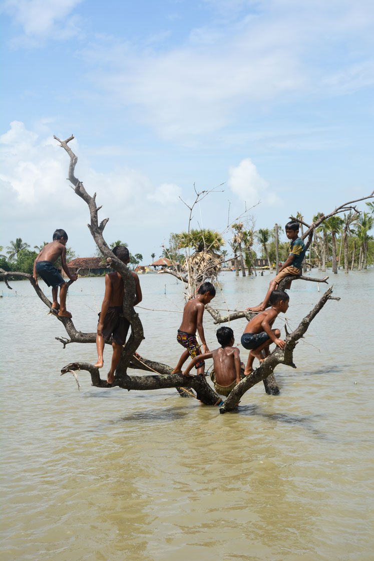 Left: Women of Kalidaspur village, Chhoto Molla Khali island, Gosaba block, returning home after collecting relief items from a local organisation. Right: Children playing during the high tide in Baliara village on Mousuni island. Their fathers work as a migrant labourers in the paddy fields of Uttarakhand.

