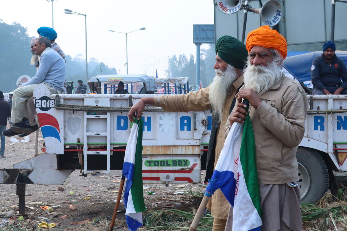 Elderly farmers using the flag poles as support while listening to the speakers at the protest site