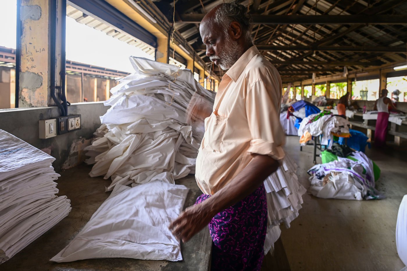 Rajan folding a pile of freshly cleaned white bed sheets