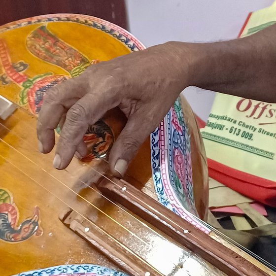 Narayanan (left) showing the changes in the structures of the veena where he uses guitar keys to tighten the strings. Plucking the strings (right)