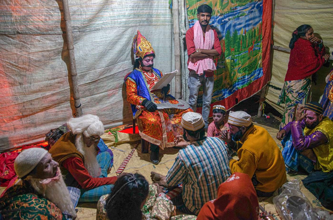 The actors rehearse their lines in the green room. Dilip Mandal sits in a chair, sword in hand, waiting for his cue to enter the stage