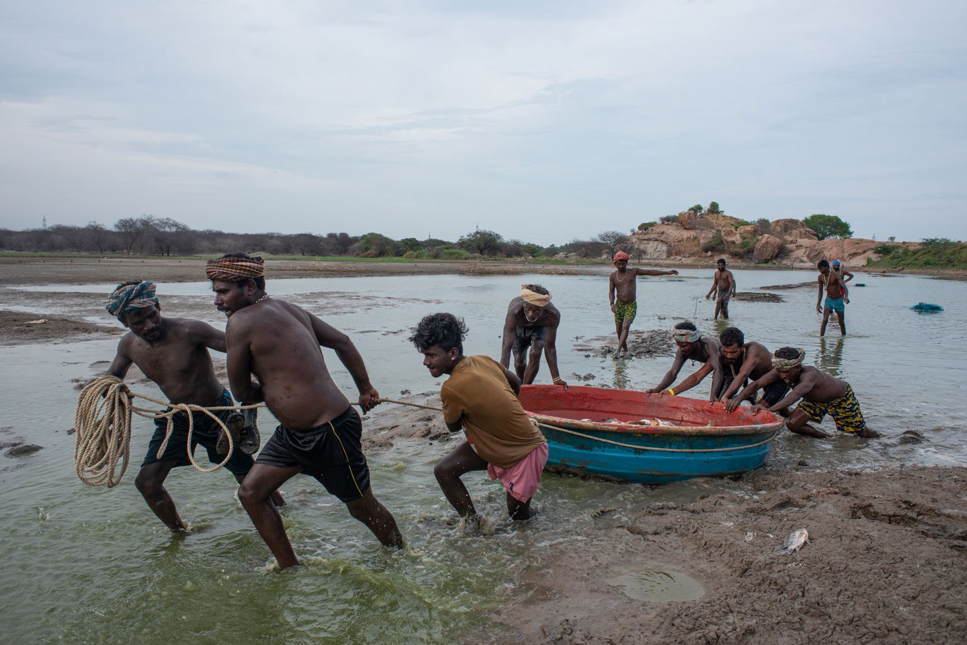 Fishermen pushing their coracle towards the shore; it is heavy and loaded with their catch