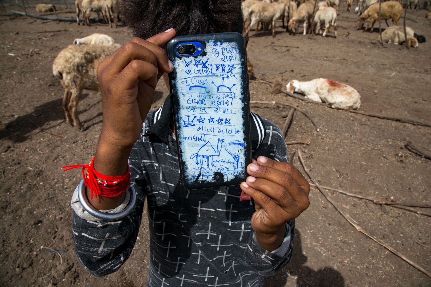 A maldhari child holds up a smartphone to take photos; the back is decorated with his doodles