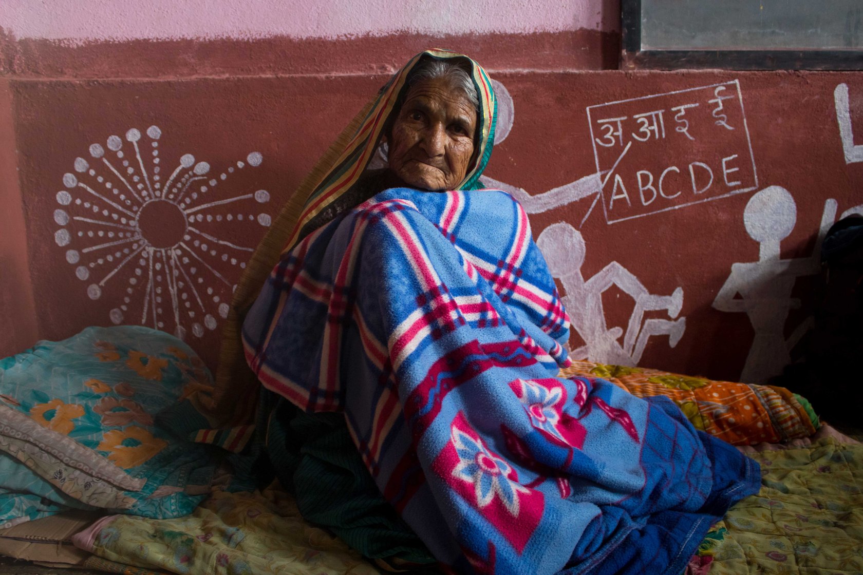 Woman shivers inside a blanket in transit camp as floods ravage Kolhapur.